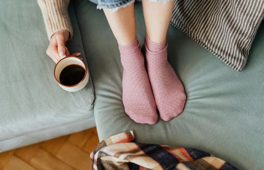 img blog Como mantener los pies hidratados en invierno Mujer sentada en el sofá con calcetines cómodos durante el invierno, protegiendo sus pies del frío y ayudando a mantenerlos hidratados.