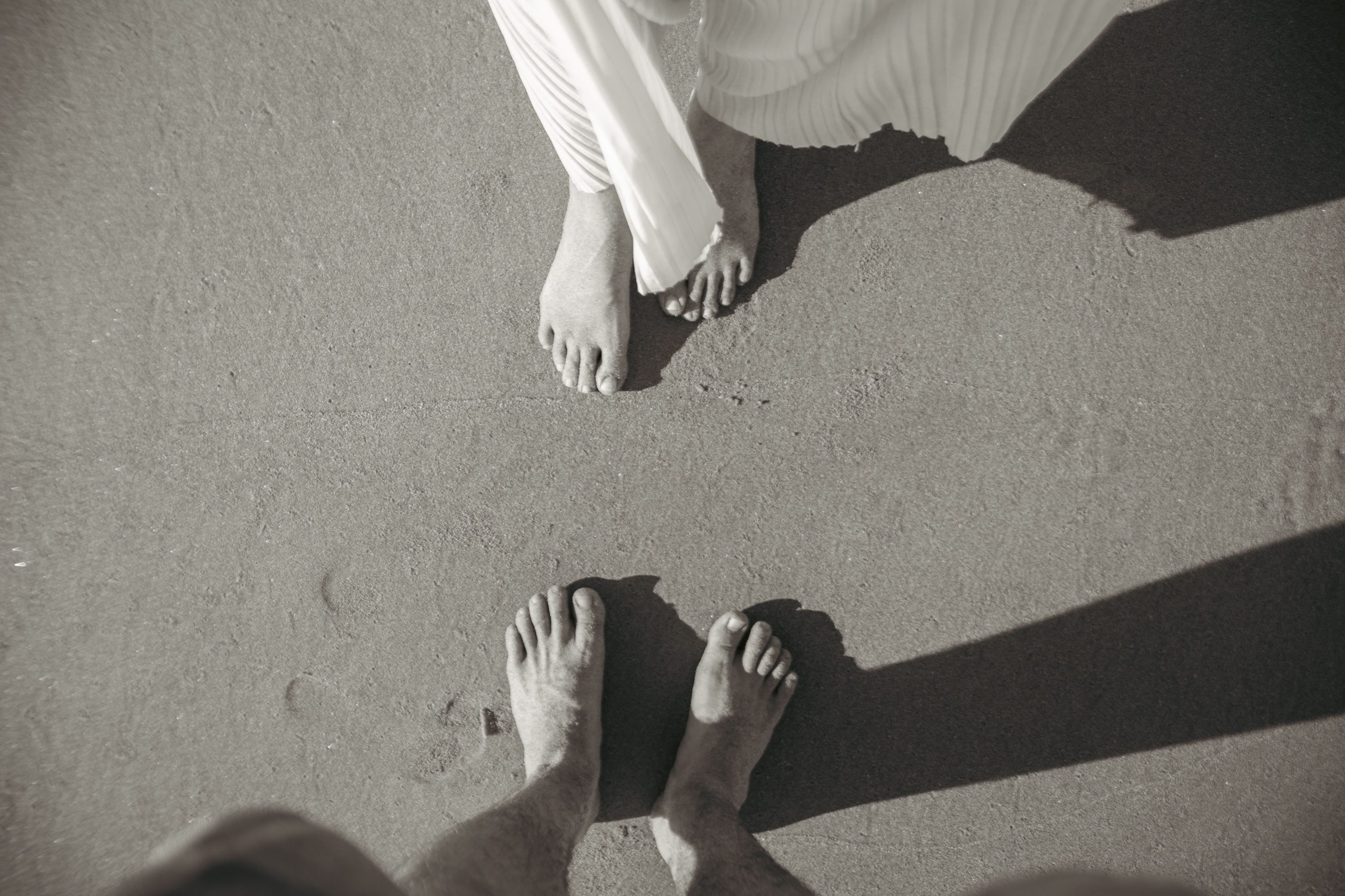 pexels photo 28232562 scaled Artistic black and white image of a couple's feet on a sandy beach, capturing a romantic moment.